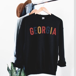 May include: Black sweatshirt with the word "GEORGIA" printed in red, blue, yellow, and orange letters.