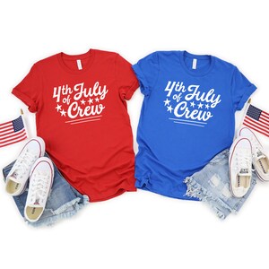 May include: Two t-shirts, one red and one blue, with the text "4th of July Crew" in white. The shirts have a white star design and are laid out on a white background.