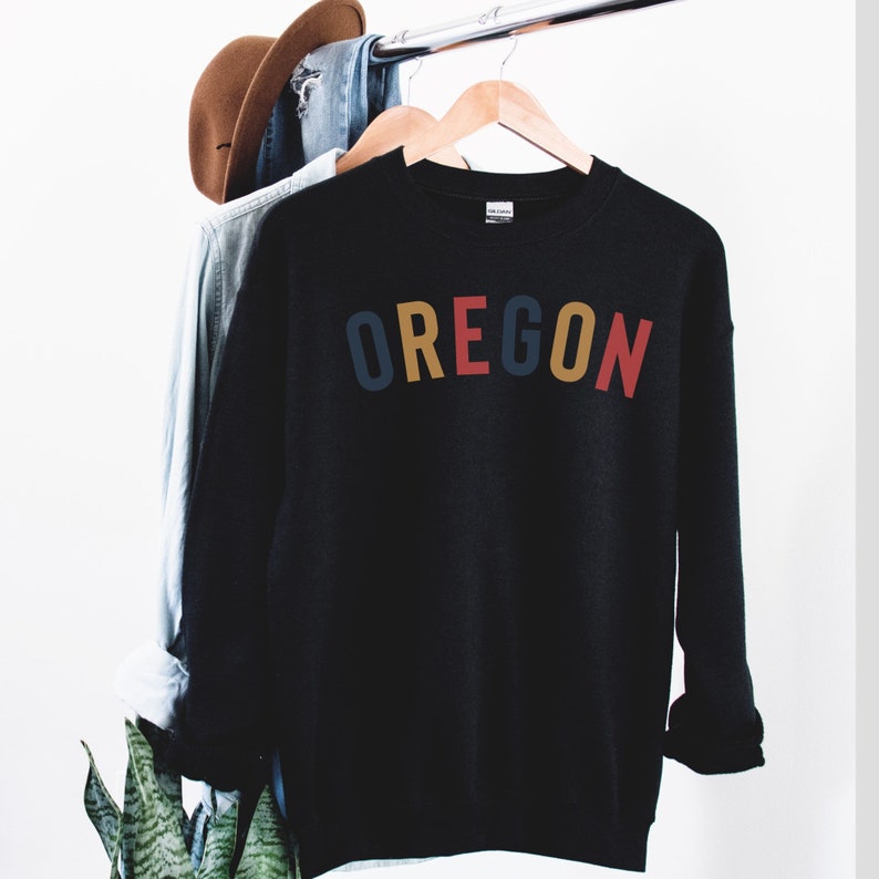 May include: Black sweatshirt with the word "OREGON" printed in colorful letters. The letters are in shades of yellow, red, and blue.
