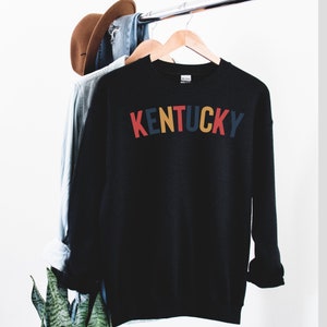 May include: Black sweatshirt with the word "KENTUCKY" printed in colourful letters. The letters are red, yellow, blue and green.