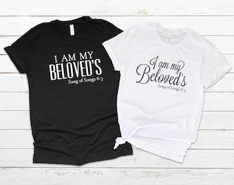 Könnte beinhalten: Zwei schwarze und weiße T-Shirts mit dem Text "I am my Beloved's Song of Songs 6:3" darauf. Ein Shirt hat den Text in einer fetten, serifenlosen Schrift, während das andere Shirt den Text in einer kursiven Schrift hat.