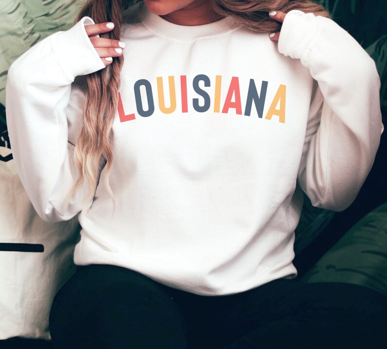 May include: White sweatshirt with the word "LOUISIANA" printed in rainbow colors across the chest.