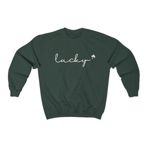以下が含まれることがあります： 暗い緑色のスウェットシャツに、白い筆記体で「lucky」という文字と、小さな白いクローバーが書かれています。