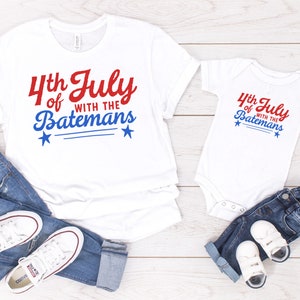 May include: White t-shirt and onesie with red and blue text that says "4th of July with the Batemans". The shirts have two small blue stars on each side of the text.