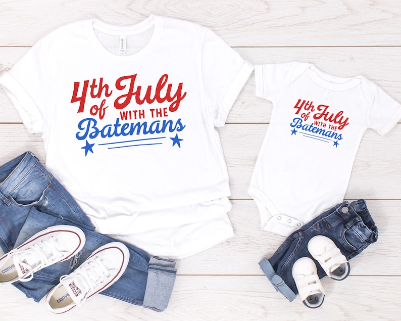 May include: White t-shirt and onesie with red and blue text that says "4th of July with the Batemans". The shirts have two small blue stars on each side of the text.