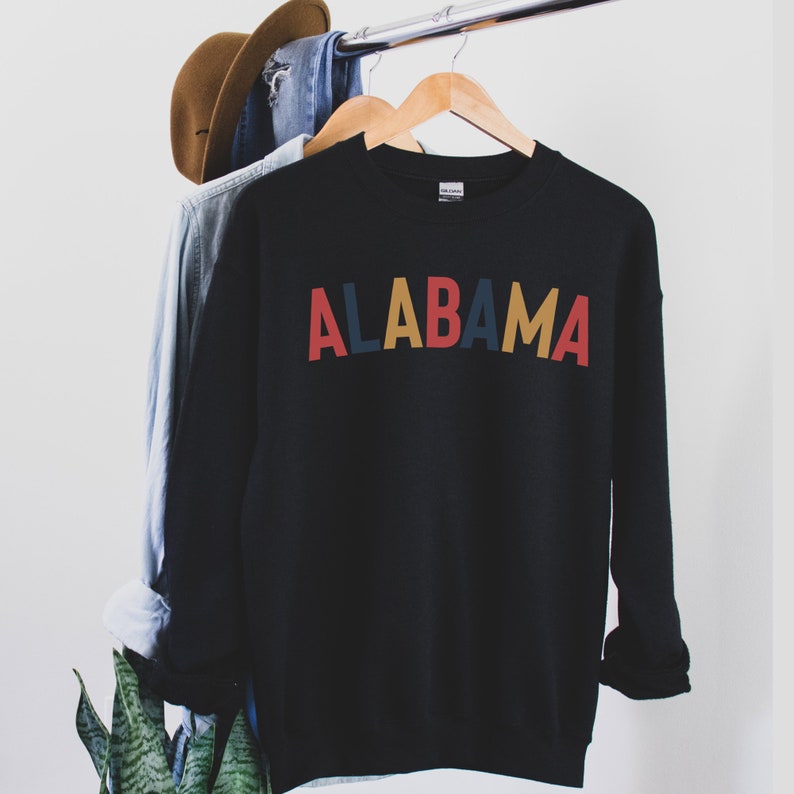 May include: Black sweatshirt with the word "ALABAMA" written in colorful letters. The letters are red, blue, yellow, and red.