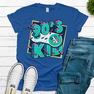 May include: A royal blue t-shirt with a graphic design of a retro video game controller and the text "90's Kid" in a colorful, pixelated font.