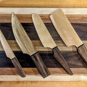 Peut inclure: Quatre couteaux à manches en bois avec différentes formes et tailles de lames sont présentés sur une planche à découper en bois avec un motif de grain de bois multicolore. La planche à découper porte le texte "WB Designs" imprimé dans le coin inférieur droit.