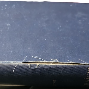 May include: A vintage, hardcover book with a dark blue cover. The spine displays gold lettering and the title "The Secret Doctrine" and the author's name. The book shows signs of wear, with frayed edges and a slightly faded cover.