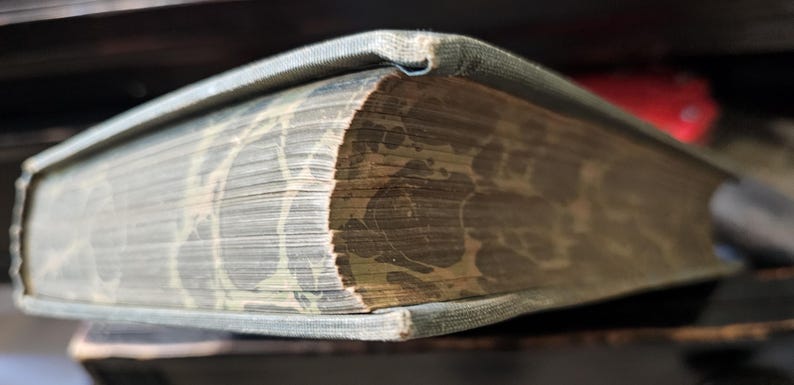 K&ouml;nnte beinhalten: Nahaufnahme des Buchr&uuml;ckens eines abgenutzten, gebundenen Buches mit einem gemusterten Einband. Das Buch ist geschlossen und der R&uuml;cken ist sichtbar, was das Alter und den Verschlei&szlig; des Buches zeigt.