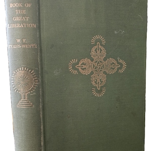 May include: A hardback book titled The Tibetan Book of the Great Liberation by W. Y. Evans-Wentz. The cover is olive green with a gold embossed cross-shaped symbol in the centre. The spine features the title and a gold circular emblem.