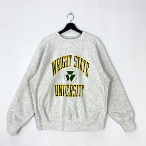 May include: A light grey heathered crewneck sweatshirt featuring the text WRIGHT STATE UNIVERSITY in dark green lettering with a yellow outline. A central dark green triangular logo is positioned between the words WRIGHT STATE and UNIVERSITY.