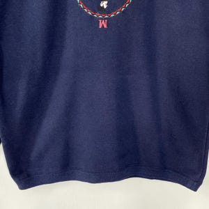 May include: Navy blue sweatshirt with an embroidered design at the top. The design includes a cartoon character and the letter "M" in pink. The sweatshirt is made of a soft material.