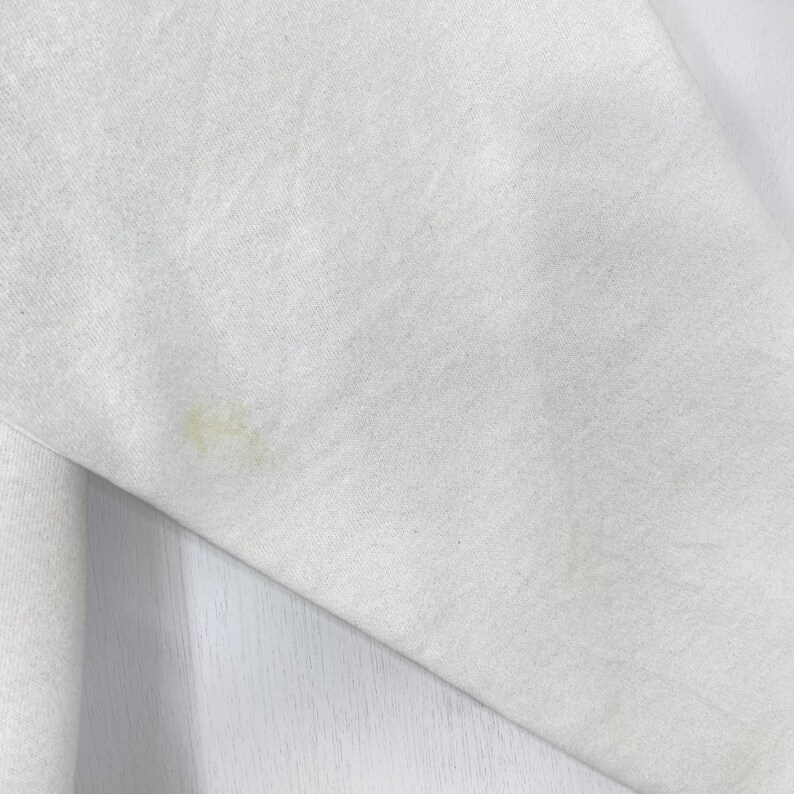 Puede incluir: Primer plano de una tela blanca con una mancha marr&oacute;n claro. La tela parece ser un material suave, posiblemente una sudadera o una prenda similar. La mancha est&aacute; ubicada en el lado inferior izquierdo de la imagen.