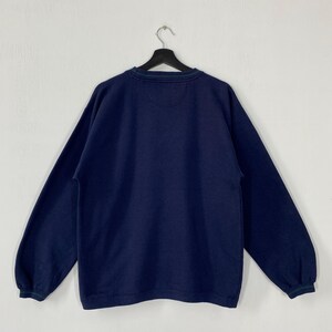 May include: Navy blue sweatshirt with a crew neck and long sleeves. The collar and cuffs have a green and navy striped trim. The back of the sweatshirt is visible, hanging from a black hanger against a white background.