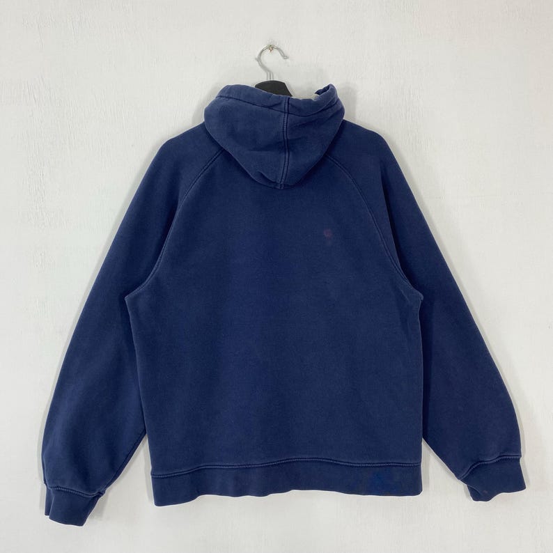 May include: A navy blue hoodie with a hood and long sleeves. The sweatshirt is hanging on a black hanger against a white background. The hoodie has a small logo on the chest.