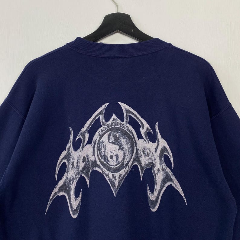 Puede incluir: Sudadera azul marino con un gran gr&aacute;fico blanco en la espalda. El gr&aacute;fico incluye el texto "T&C Surf Designs" y un emblema estilizado. La sudadera est&aacute; colgada de una percha negra.