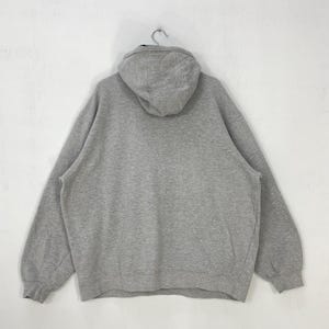 May include: A gray oversized hoodie with a hood, hanging from a metal hook. The back of the sweatshirt is visible, showing the hood and the body of the garment. The fabric appears to be a soft, comfortable material, suitable for casual wear.