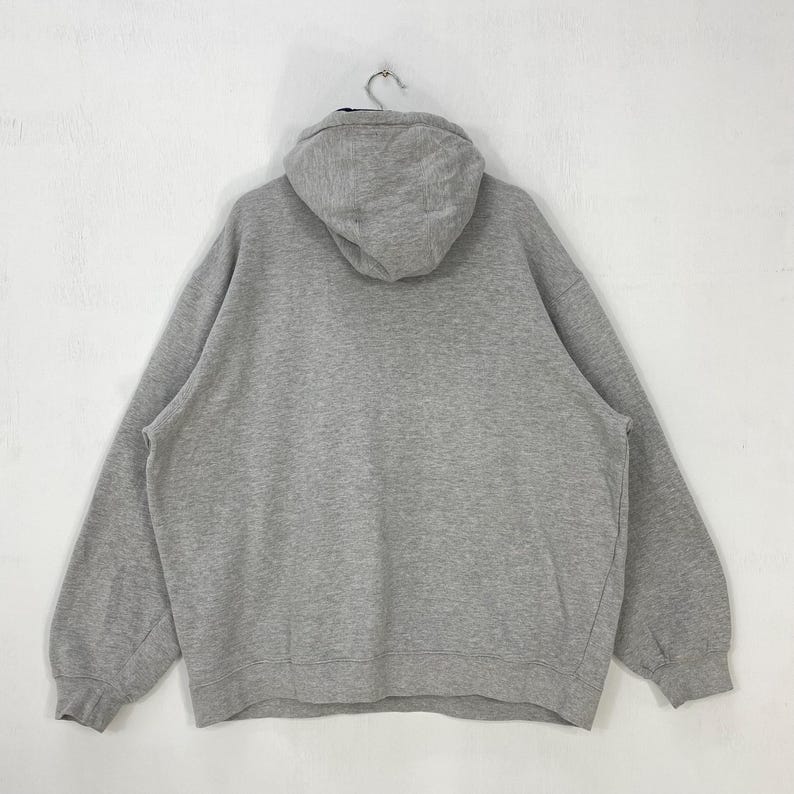 May include: A gray oversized hoodie with a hood, hanging from a metal hook. The back of the sweatshirt is visible, showing the hood and the body of the garment. The fabric appears to be a soft, comfortable material, suitable for casual wear.