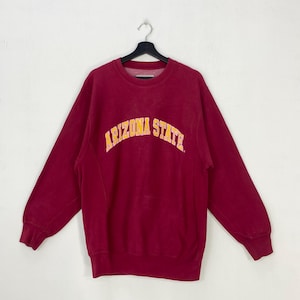 May include: A maroon sweatshirt with the text "ARIZONA STATE" in yellow and orange arched across the chest. The sweatshirt has long sleeves and a crew neck. The garment is hanging on a black hanger.