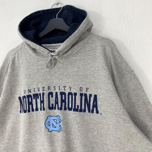 May include: A gray hooded sweatshirt with the words "UNIVERSITY OF NORTH CAROLINA" in navy blue across the chest. The sweatshirt has a light blue logo of a stylized letter "N" and "C" intertwined. The hood is lined with navy blue fabric.