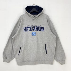 May include: A gray hooded sweatshirt with the text "UNIVERSITY OF NORTH CAROLINA" in navy blue. The sweatshirt has a navy blue lined hood and a front pocket. A light blue logo is below the text.