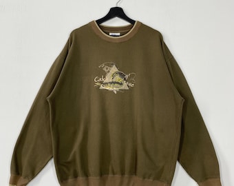 May include: Olive green sweatshirt with a crew neck and long sleeves. The front features an embroidered design of a fish, fishing rod, and the words "Catch & Release". The collar and cuffs are a darker brown.