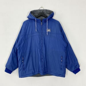 May include: A blue Adidas hooded jacket with a full-length zipper, two side pockets, and a small logo on the chest. The jacket has a gray hood lining and blue cuffs. The jacket is hanging on a black hanger.