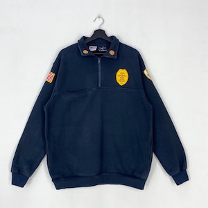 May include: A navy blue quarter-zip pullover sweatshirt featuring a yellow shield-shaped patch on the chest that reads Chief Northlake Fire Dept IL. The garment includes a small American flag patch on the right sleeve and a circular patch on the left.