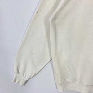 Pu&ograve; includere: Felpa color crema con polsini e orlo a coste. La manica presenta diverse macchie marroni. Il tessuto sembra essere un materiale morbido a maglia. La felpa &egrave; un capo casual per tutti i giorni.
