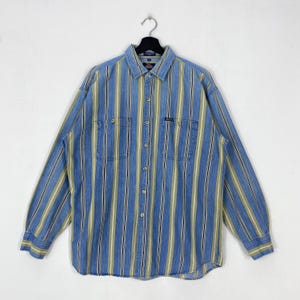 May include: A long-sleeve button-down shirt featuring a vertical striped pattern in shades of blue, light green, and white. The shirt includes a standard collar, two chest pockets with button closures, and a central button placket down the front.