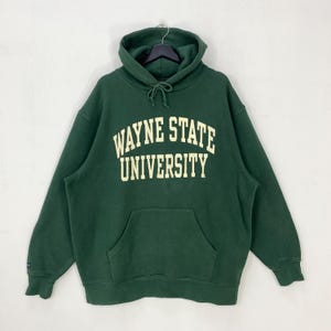 May include: A dark green Wayne State University hooded sweatshirt with a front pocket and drawstring hood. The university's name is printed in a cream-coloured, block-style font across the chest. The sweatshirt is hanging on a black hanger.