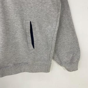 May include: A close-up of a gray sweatshirt with a dark blue pocket. The sweatshirt has a ribbed cuff and a simple, classic design. The fabric appears to be a soft, comfortable material.