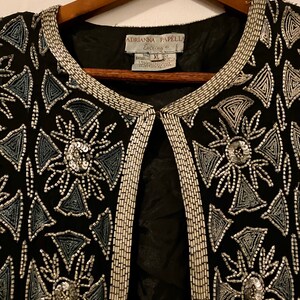 May include: A black beaded jacket with silver and blue beading in a geometric pattern. The label reads "Adrianna Papell Evening" and "Size XL".