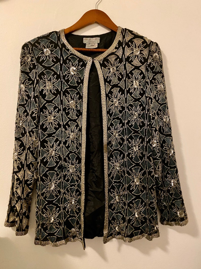 May include: A black beaded jacket with a silver and blue geometric pattern. The jacket has a front closure and long sleeves.