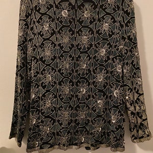May include: A black long-sleeved top with a silver and blue geometric pattern. The top is fully beaded and has a round neckline.