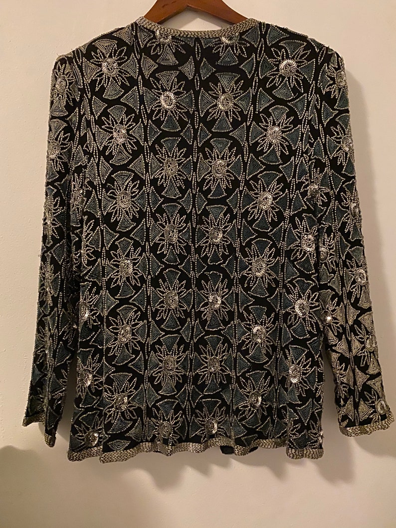 May include: A black long-sleeved top with a silver and blue geometric pattern. The top is fully beaded and has a round neckline.