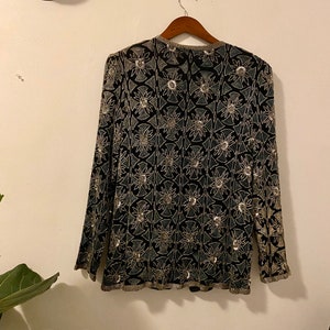 May include: A black long-sleeved top with a silver floral pattern. The top is beaded and has a V-neck.