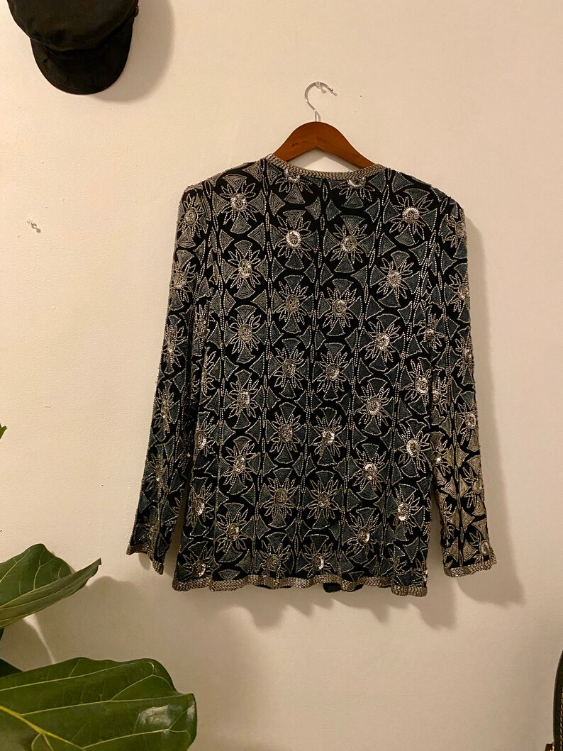 May include: A black long-sleeved top with a silver floral pattern. The top is beaded and has a V-neck.