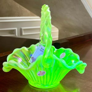 Può includere: Un vivace cestino di vetro verde con un manico attorcigliato. Il cestino ha un bordo a balze e un'etichetta con la scritta "Basket - FENT". Il cestino è contrassegnato "Retired Handmade in U.S.A."