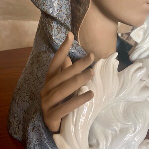 May include: A ceramic figurine of a woman wearing a blue and brown robe, holding a white ceramic dog.
