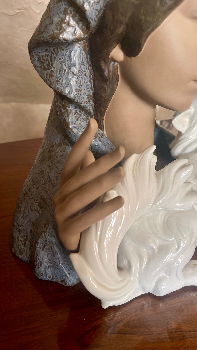May include: A ceramic figurine of a woman wearing a blue and brown robe, holding a white ceramic dog.