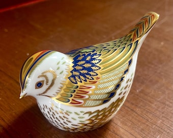 Puede incluir: Figurita decorativa de cerámica con forma de pájaro. El ave presenta una base blanca con intrincados detalles pintados en oro, azul, verde y rojo. El diseño incluye patrones en las alas y la cola, con un pico y detalles en los ojos dorados. Un artículo de colección.