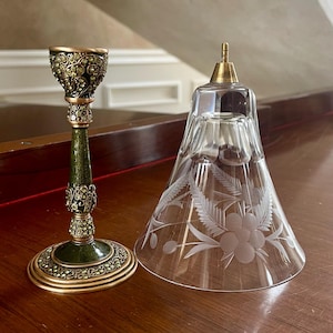 May include: An ornate candlestick with a green and gold base and stem, and a clear glass bell-shaped shade with etched floral designs. The candlestick has intricate detailing.