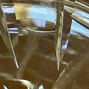 K&ouml;nnte beinhalten: Nahaufnahme eines transparenten, geschliffenen Glasobjekts mit scharfen, kantigen Facetten. Das Glas reflektiert das Licht und erzeugt helle Reflexe und Schatten. Das Design weist eine Reihe spitzer, dreieckiger Formen auf. Der Gesamteffekt ist einer von Eleganz und Pr&auml;zision.