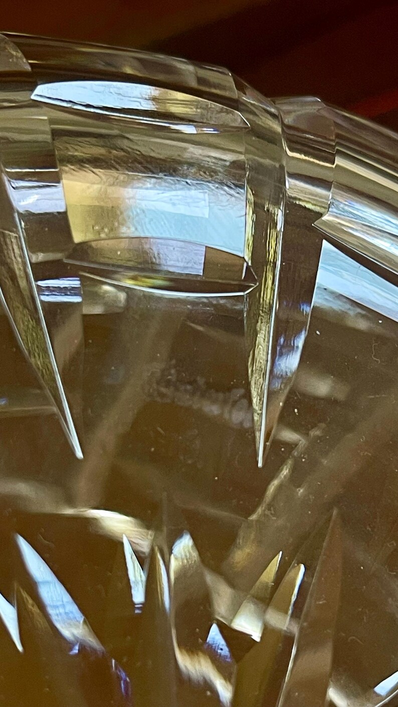 K&ouml;nnte beinhalten: Nahaufnahme eines transparenten, geschliffenen Glasobjekts mit scharfen, kantigen Facetten. Das Glas reflektiert das Licht und erzeugt helle Reflexe und Schatten. Das Design weist eine Reihe spitzer, dreieckiger Formen auf. Der Gesamteffekt ist einer von Eleganz und Pr&auml;zision.