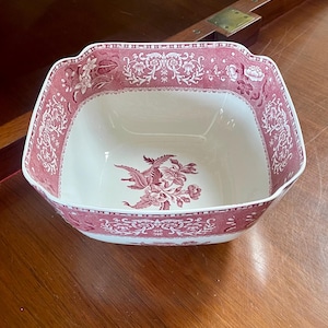 May include: A square ceramic bowl featuring a cream-coloured interior and a deep pink exterior. The exterior and the centre of the bowl are decorated with a detailed floral pattern in a matching deep pink tone, featuring intricate botanical motifs.