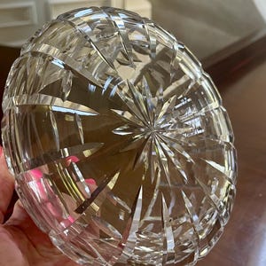 K&ouml;nnte beinhalten: Klarer, geschliffener Glasnapf mit Sternmuster am Boden. Die Schale hat eine abgerundete Form und eine strukturierte Oberfl&auml;che, die das Licht reflektiert. Die Schale wird in einer Hand gehalten.