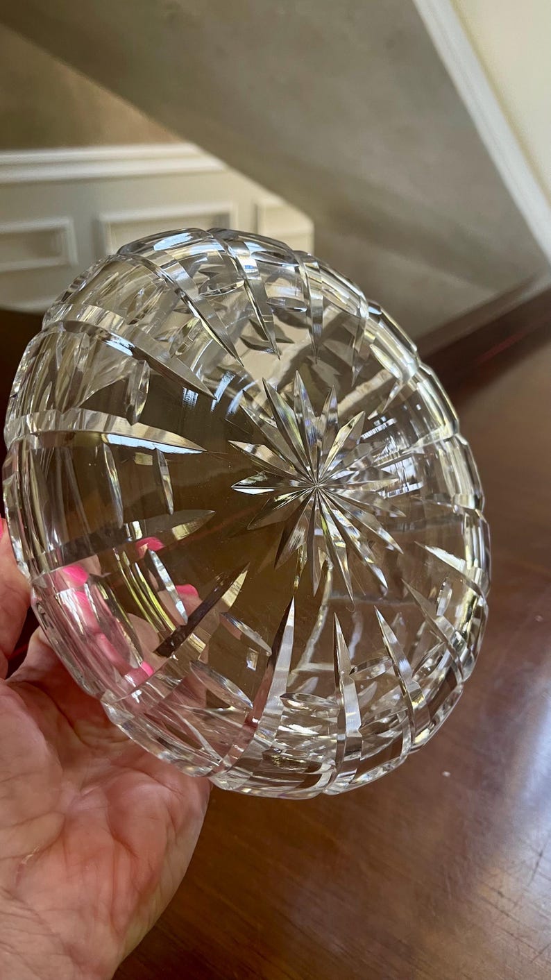 K&ouml;nnte beinhalten: Klarer, geschliffener Glasnapf mit Sternmuster am Boden. Die Schale hat eine abgerundete Form und eine strukturierte Oberfl&auml;che, die das Licht reflektiert. Die Schale wird in einer Hand gehalten.