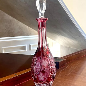 Puede incluir: Una jarra de cristal rojo rubí con tapón transparente. La jarra presenta un diseño floral y mide aproximadamente 30 cm de altura. El cristal está tallado con intrincados patrones, lo que aumenta su elegancia. Una pieza decorativa para el hogar.
